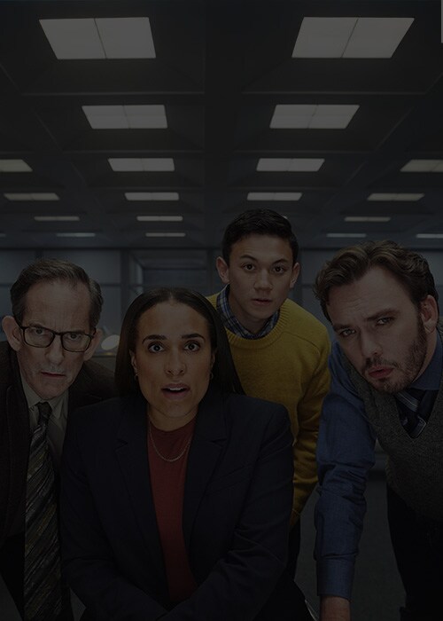 Four office employees intensely looking at a computer screen in a dimly lit modern office space