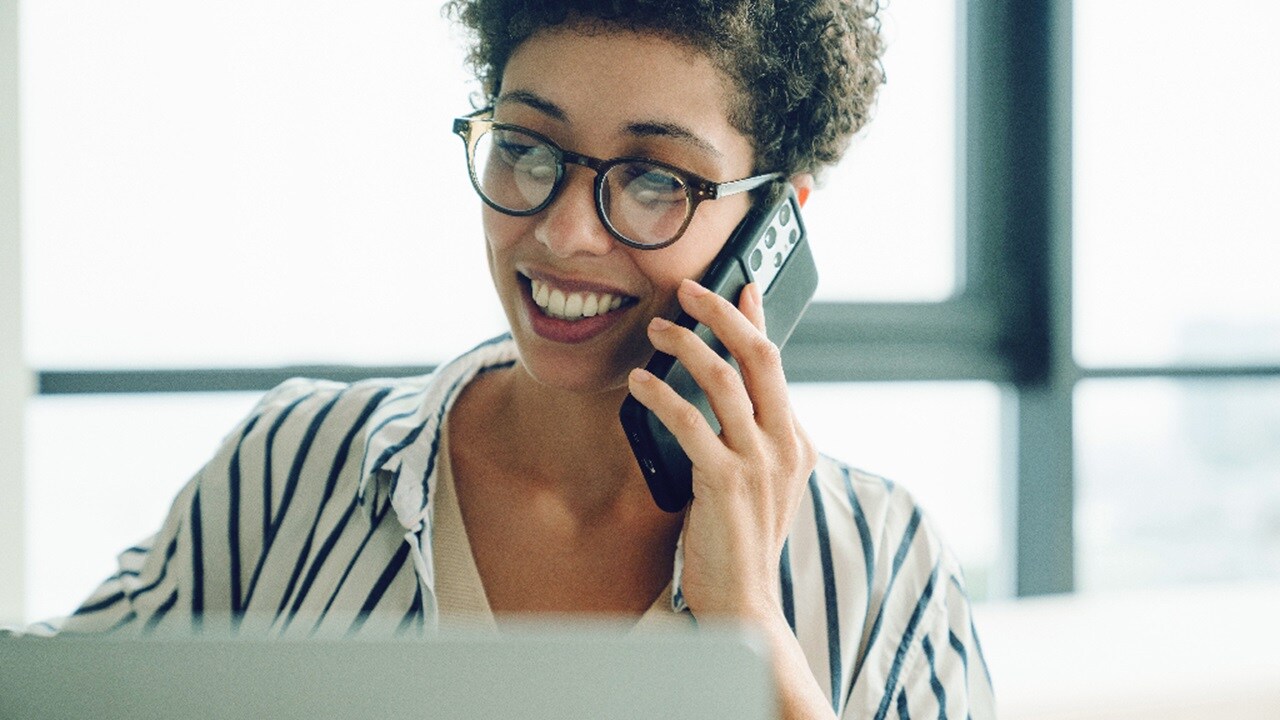Female smiling while talking on the mobile phone in front of desktop screen