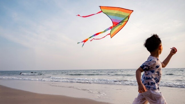 A boy joyfully flying a colorful kite against a clear blue sky.