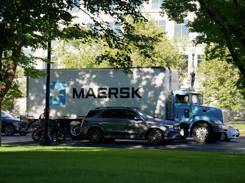 Workers unloading Maersk delivery truck on a city sidewalk.