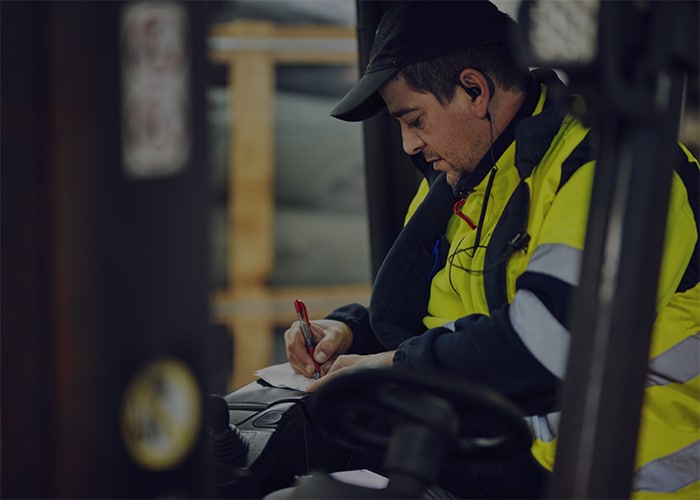 Man wearing yellow jacket on the forklift writing on notepad