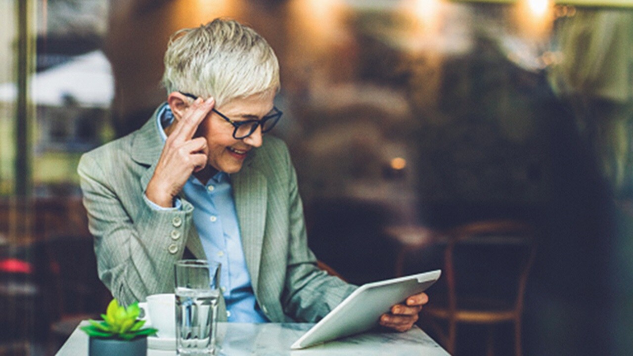 A smiling woman with glasses looking at their tablet.