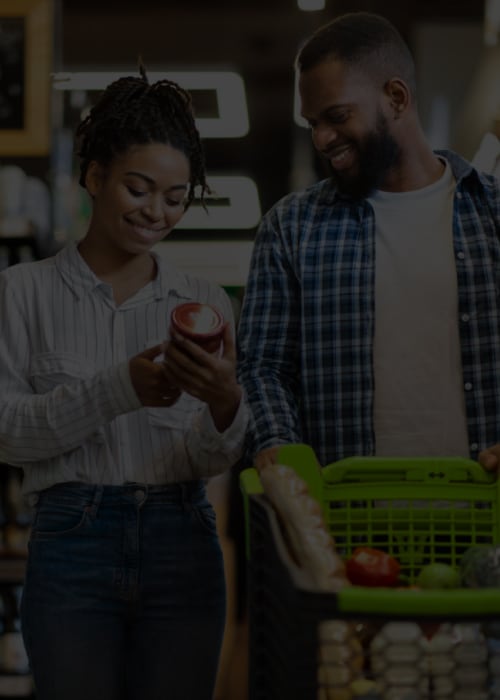 A man and woman reviewing packaged goods on supermarket shelves.