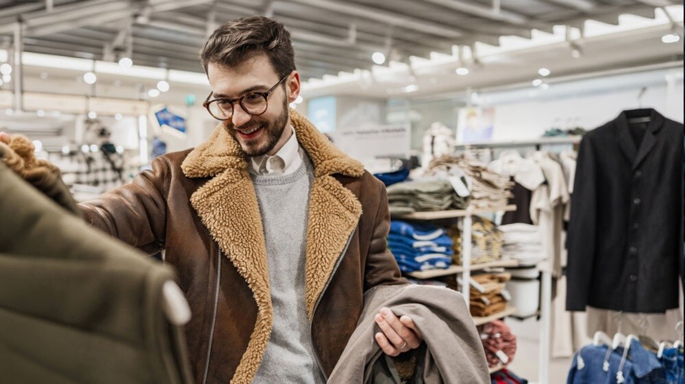 A man examines a jacket while standing in a clothing store.