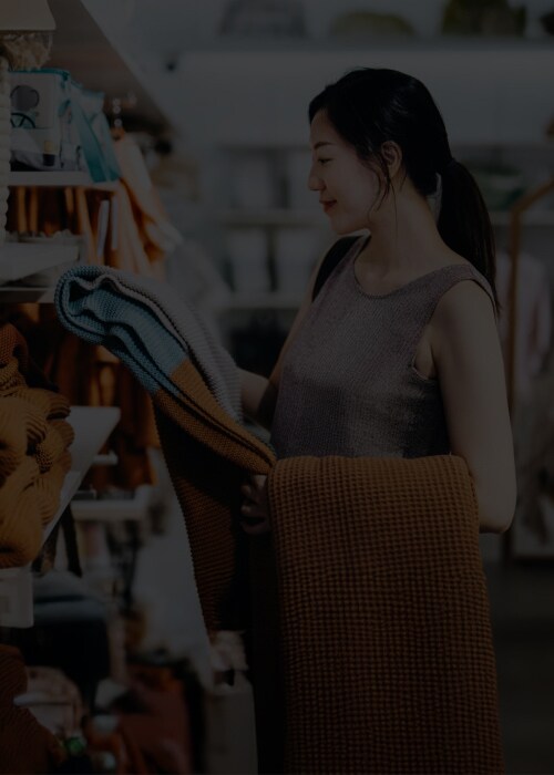 A woman browsing clothes in a store, thoughtfully assessing garments on the racks.